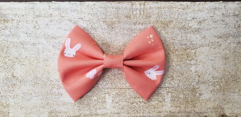 May include: A coral pink bow with a white bunny rabbit print. The bow has a small white center.