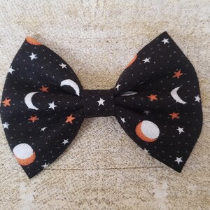 May include: A black fabric bow with a white and orange moon and star pattern.