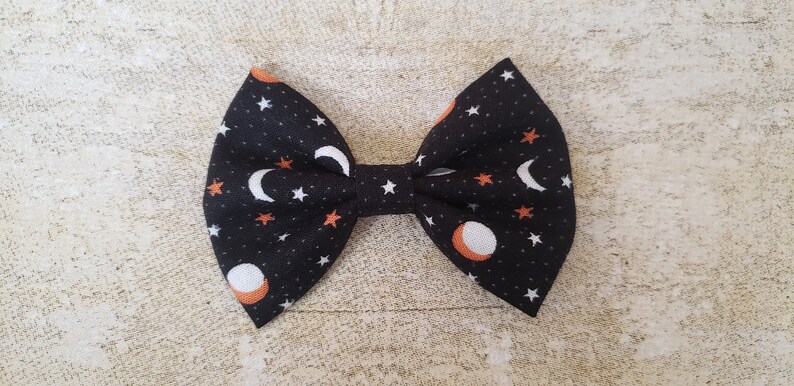 May include: A black fabric bow with a white and orange moon and star pattern.