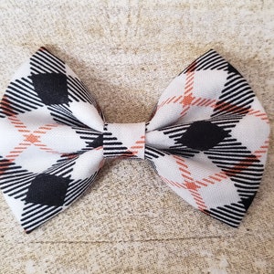May include: A white bow with a black and orange plaid pattern.