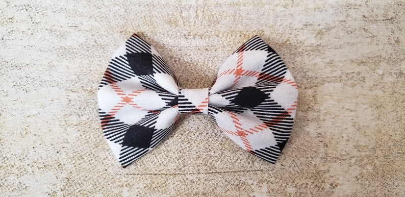 May include: A white bow with a black and orange plaid pattern.