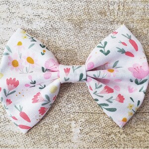 May include: A white fabric bow with a pink and green floral pattern. The bow is tied in a classic shape with a center loop.