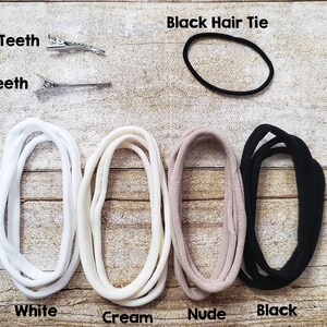 Puede incluir: Un surtido de accesorios para el cabello, que incluye una goma negra, dos horquillas plateadas y cuatro lazos de tela en blanco, crema, nude y negro. Dispuestos sobre una superficie de madera.