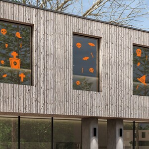 Puede incluir: Tres ventanas en una casa de madera con calcomanías naranjas de temática de Halloween. Las calcomanías incluyen calaveras, murciélagos, huesos cruzados, un sombrero de bruja y una lápida.