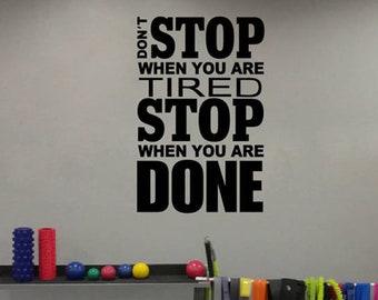 May include: Black and white motivational quote on a gray wall that reads "Don't stop when you are tired, stop when you are done". The wall is in a gym with various exercise equipment, including kettlebells, resistance bands, and foam rollers.