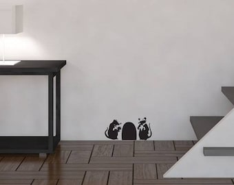 May include: A black silhouette of three mice peeking out of a hole in a white wall. The wall is in a room with a wooden floor, a black side table, and a white staircase.