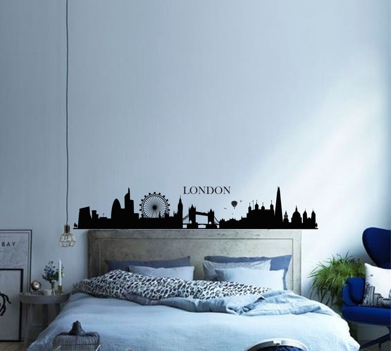 May include: Black and white silhouette of the London skyline with the London Eye, Big Ben, and Tower Bridge. The skyline is on a wall above a bed with blue bedding and a leopard print throw pillow.