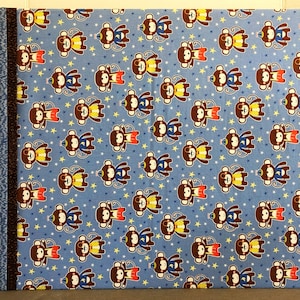 Könnte beinhalten: Blauer Stoff mit einem sich wiederholenden Muster aus braunen Affen, die gelbe und rote Hüte sowie blaue und weiße Hüte tragen. Die Affen sind von gelben Sternen umgeben.