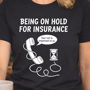 May include: Black t-shirt with white text that reads "BEING ON HOLD FOR INSURANCE." A white graphic of a phone receiver with a speech bubble saying "Your call is important to us." An hourglass graphic is also present.