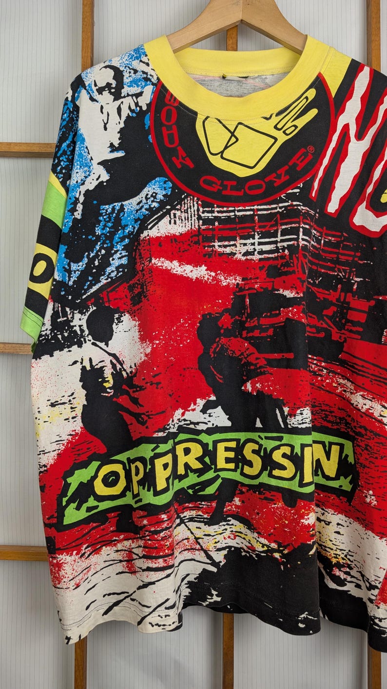 Pu&ograve; includere: T-shirt grafica vintage con colletto e maniche gialle. La maglietta presenta un design colorato con le parole "BODY GLOVE" e "OPPRESSIN" in un carattere audace in stile graffiti. Il design include elementi rossi, neri, bianchi, blu e verdi.