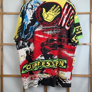 Pu&ograve; includere: Una maglietta vintage e colorata con un design grafico audace. La maglietta presenta un colletto e maniche gialle, con un vivace mix di arte astratta rossa, nera, bianca e blu. Il testo "BODY GLOVE" e "OPPRESSSN" &egrave; visibile.