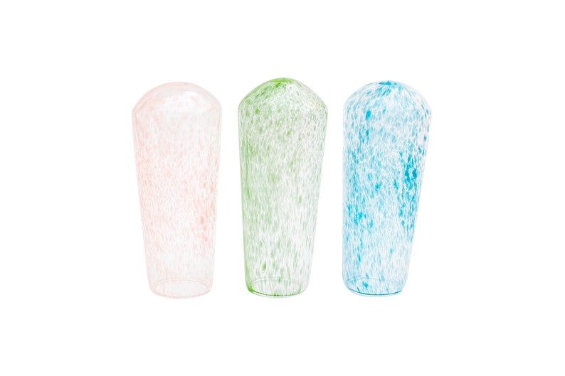 May include: Three tall, speckled glass vases in pastel colors. The vases are cylindrical with rounded tops. One is pink, one is green, and one is blue. The speckled pattern is white. The vases are suitable for home decor.