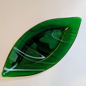 May include: A green glass leaf-shaped dish with white and gold swirls. The dish is ideal for serving snacks or holding jewellery.