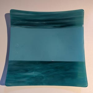 May include: Square glass dish in teal and turquoise. The top and bottom sections have a marbled effect, while the centre is a solid turquoise. The dish has rounded corners and a smooth surface.