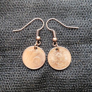 May include: A pair of copper-colored earrings with a 1 Euro coin charm. The coins are from the European Union and feature a stylized portrait of a woman.