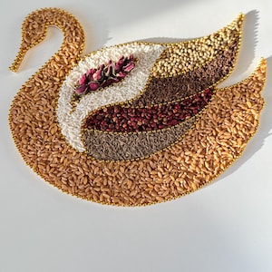 May include: A swan-shaped mosaic art piece, crafted from various grains and seeds in shades of brown, white, and red. The swan's outline is adorned with golden beads, and a cluster of dried flowers rests on its body. The artwork is set against a white background.