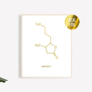 Könnte beinhalten: Gerahmter Druck mit einem goldfarbenen Molekülstrukturdiagramm mit der Aufschrift "WHISKEY". Das Diagramm befindet sich auf weißem Hintergrund, mit einem Goldfoliensiegel in der oberen rechten Ecke. Der Druck ist in einem hellen Rahmen.