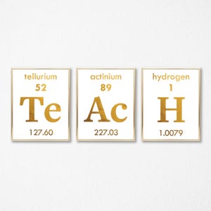 以下が含まれることがあります： テルル（Te）、アクチニウム（Ac）、水素（H）の化学元素記号が書かれた、金色の額縁付きのプリントが3枚あります。原子番号と原子量も含まれています。