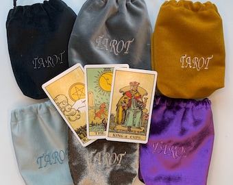 May include: Five velvet bags in different colors, each with the word "Tarot" embroidered on the front. The bags are arranged around a tarot card with the image of the King of Cups.
