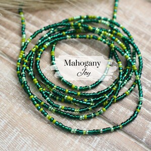 May include: A green and gold beaded waist chain, also known as a waist bead or belly chain. The chain is made of small, round beads and is designed to be worn around the waist.