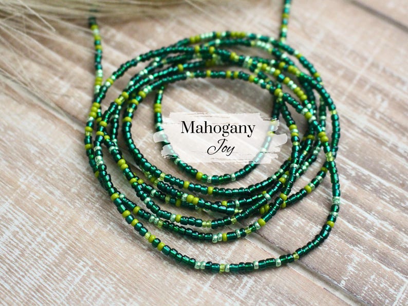 May include: A green and gold beaded waist chain, also known as a waist bead or belly chain. The chain is made of small, round beads and is designed to be worn around the waist.
