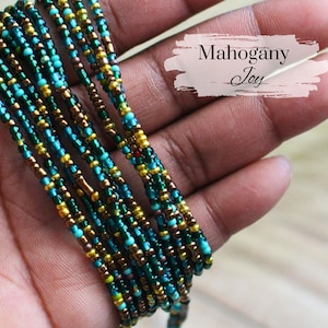 May include: Strands of colorful beads in teal, gold, and brown are held in a hand. The beads are tightly strung together, creating a layered effect. The text "Mahogany Joy" is displayed on the image.