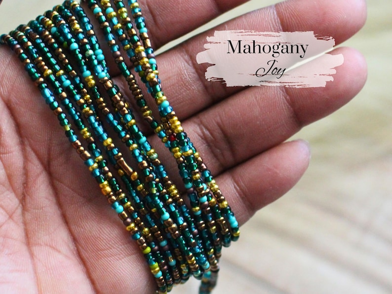 May include: Strands of colorful beads in teal, gold, and brown are held in a hand. The beads are tightly strung together, creating a layered effect. The text "Mahogany Joy" is displayed on the image.