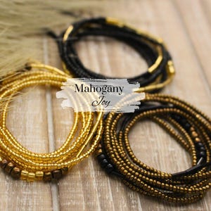 May include: An overhead shot displays three beaded waist chains in gold and black. The gold chains have a mix of gold and brown beads. The black chain has gold accents. The text "Mahogany Joy" is in the center.