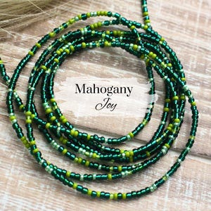 May include: A green and gold beaded necklace with the text "Mahogany Joy" on a white background.
