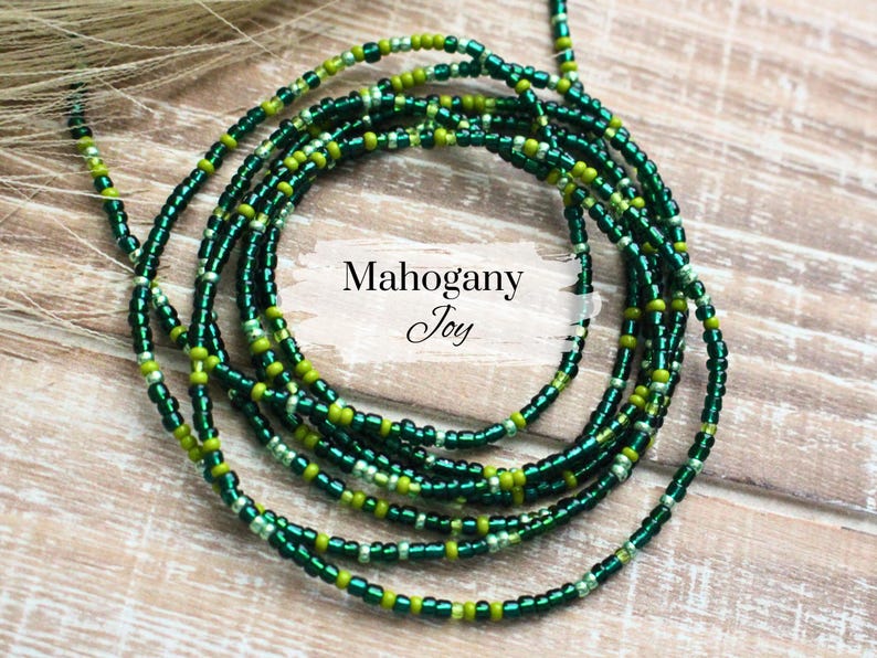 May include: A green and gold beaded necklace with the text "Mahogany Joy" on a white background.