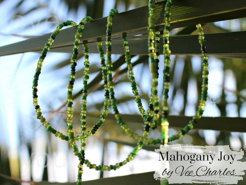May include: A green and yellow beaded necklace with the text "Mahogany Joy by Vee Charles" on a white background.