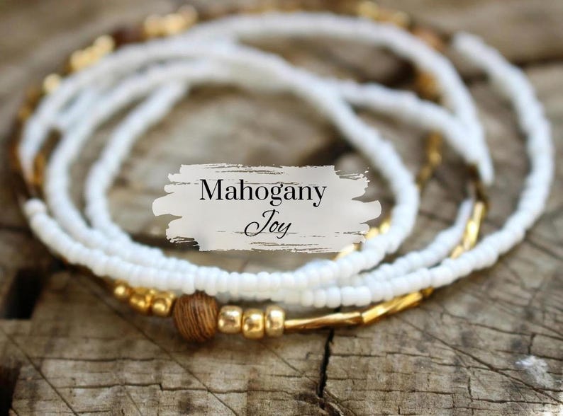 May include: White beaded necklace with gold and brown beads. The necklace is layered and has a "Mahogany Joy" label.