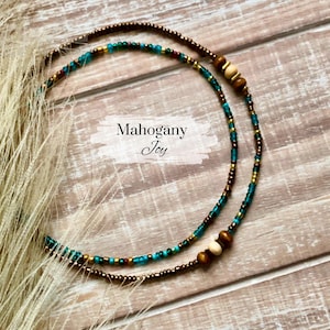 May include: A double-strand beaded necklace with brown, gold, and teal beads. The necklace has wooden beads and the text "Mahogany Joy" is visible.