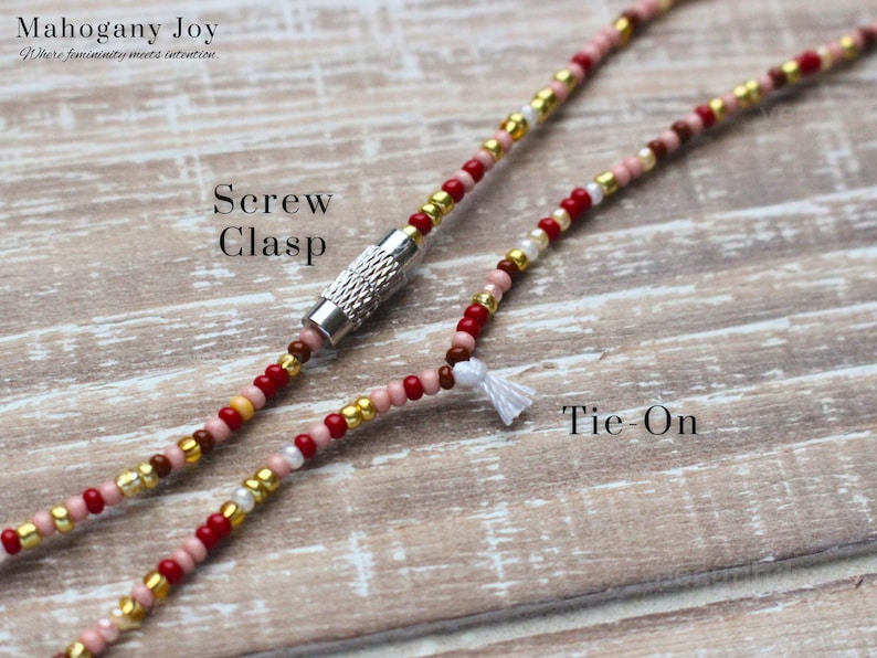 May include: Close-up of a beaded necklace with a screw clasp and tie-on closure. The necklace features red, gold, pink, and white beads. The text "Mahogany Joy" and "Screw Clasp" and "Tie-On" are visible.