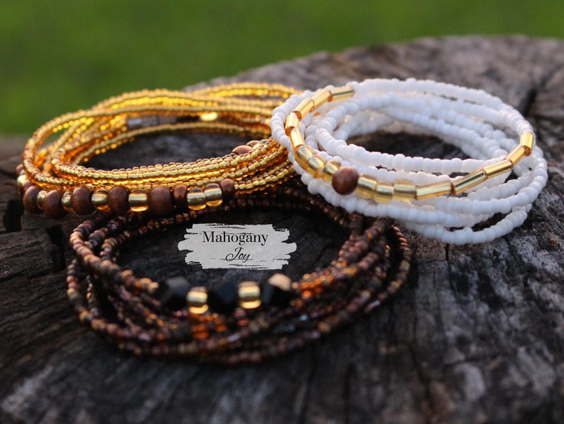 May include: Three sets of beaded bracelets in gold, white, and brown with black beads. The bracelets are stacked on top of each other and the text "Mahogany Joy" is visible in the image.