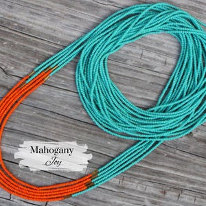 May include: A long necklace made of orange and turquoise beads. The necklace is layered and has a gold accent. The text "Mahogany Joy" is visible in the image.