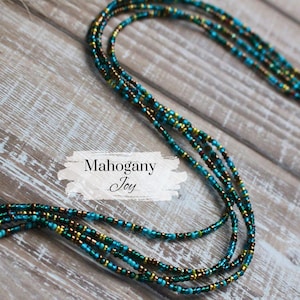 May include: A multi-strand beaded necklace in shades of teal, gold, and brown. The necklace is displayed on a rustic wooden surface. The text "Mahogany Joy" is displayed on the image.