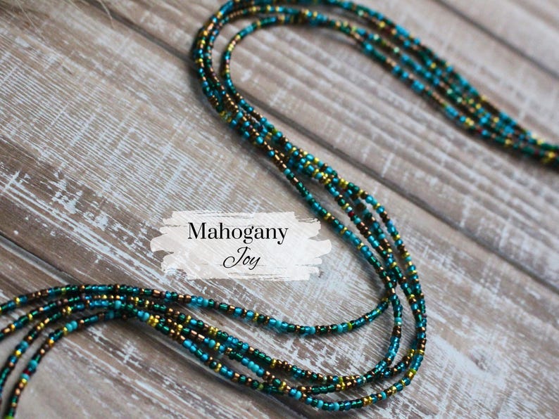 May include: A multi-strand beaded necklace in shades of teal, gold, and brown. The necklace is displayed on a rustic wooden surface. The text "Mahogany Joy" is displayed on the image.