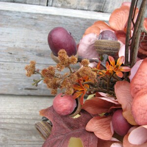 May include: A fall-themed arrangement featuring a variety of faux leaves, flowers, and acorns in shades of brown, pink, and red. The arrangement is displayed in a yellow ceramic container.