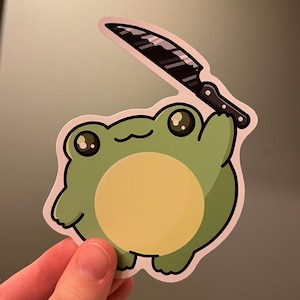 May include: A sticker depicting a cartoon frog with a light green body, a yellow belly, and large eyes. The frog is holding a black knife with a silver blade, creating a humorous and edgy aesthetic.