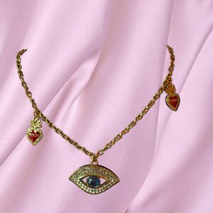 May include: Gold chain necklace with a blue evil eye pendant and two red heart charms.