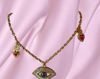 May include: Gold chain necklace with a blue evil eye pendant and two red heart charms.