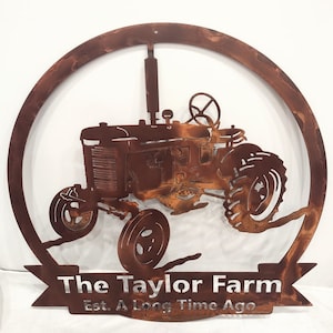May include: A rustic metal sign featuring a tractor silhouette within a circular frame. The sign is a warm, rusty brown color and includes the text "The Taylor Farm" and "Est. A Long Time Ago". The tractor has detailed wheels and a steering wheel.
