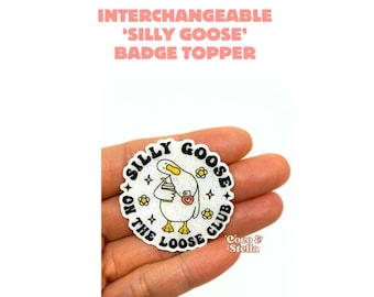 May include: A white, circular badge topper with the text "SILLY GOOSE ON THE LOOSE CLUB". The badge features a cartoon goose holding a drink and flowers. The text "INTERCHANGEABLE 'SILLY GOOSE' BADGE TOPPER" is at the top.