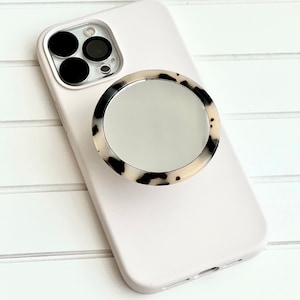 May include: A white phone case with a black and white tortoiseshell phone grip with a mirror.
