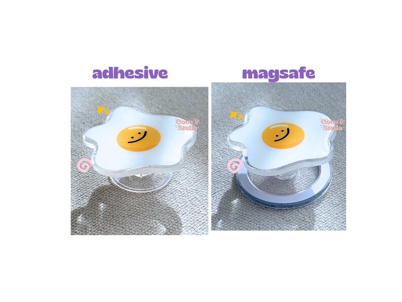 May include: Clear phone grip with a white, egg-shaped design and a yellow yolk with a smiling face. The text "adhesive" and "magsafe" are above the grips. The brand name "Coco & Stella" is also visible.