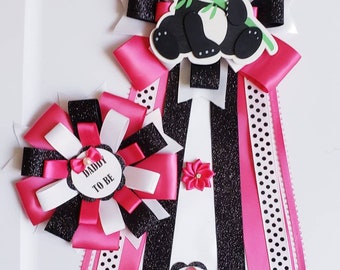 May include: Two black, white, and pink baby shower sashes with bows. One sash has a panda bear with a green bamboo shoot in its mouth. The other sash has a black and white polka dot ribbon and a white tag that says "Daddy to Be".