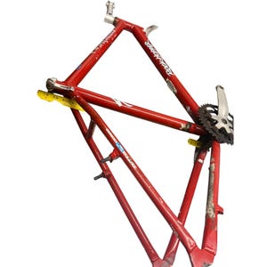Puede incluir: Un cuadro de bicicleta rojo con el texto "Rockhopper" en letras blancas. El cuadro tiene un juego de bielas plateado y una cinta m&eacute;trica amarilla. El cuadro es de metal y presenta desgaste.
