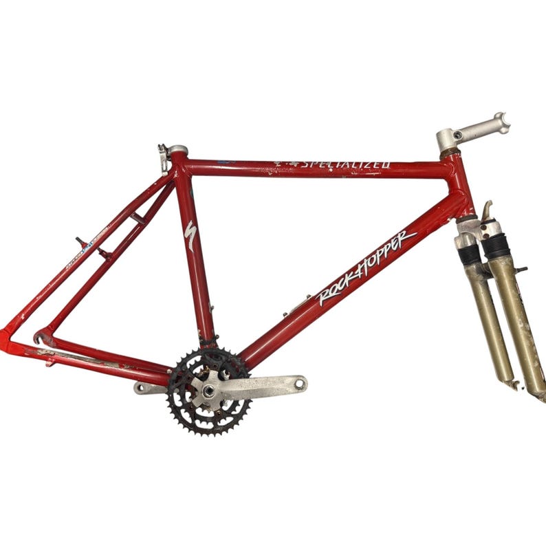 Puede incluir: Un cuadro de bicicleta Specialized Rockhopper rojo con un juego de bielas plateado y horquillas de suspensi&oacute;n delantera. El cuadro tiene el logotipo de Specialized y el texto Rockhopper en blanco. El cuadro de la bicicleta se muestra sobre un fondo blanco.