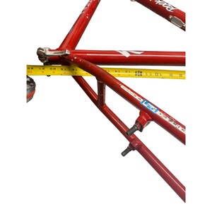 Puede incluir: Cuadro de bicicleta rojo con una cinta m&eacute;trica amarilla que muestra una medida de aproximadamente 25 cm. El cuadro tiene calcoman&iacute;as blancas y azules y est&aacute; sobre un fondo blanco. El cuadro es de metal.